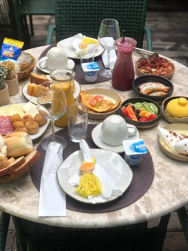 Une table ronde est dressée pour un copieux petit-déjeuner avec des viennoiseries, des fruits et des boissons.