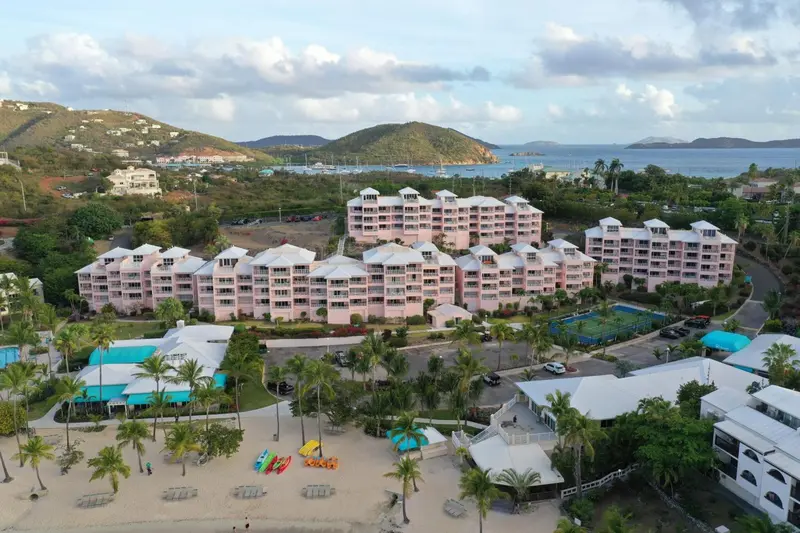 Vue aérienne d'un complexe hôtelier rose bordant une plage de sable blanc.