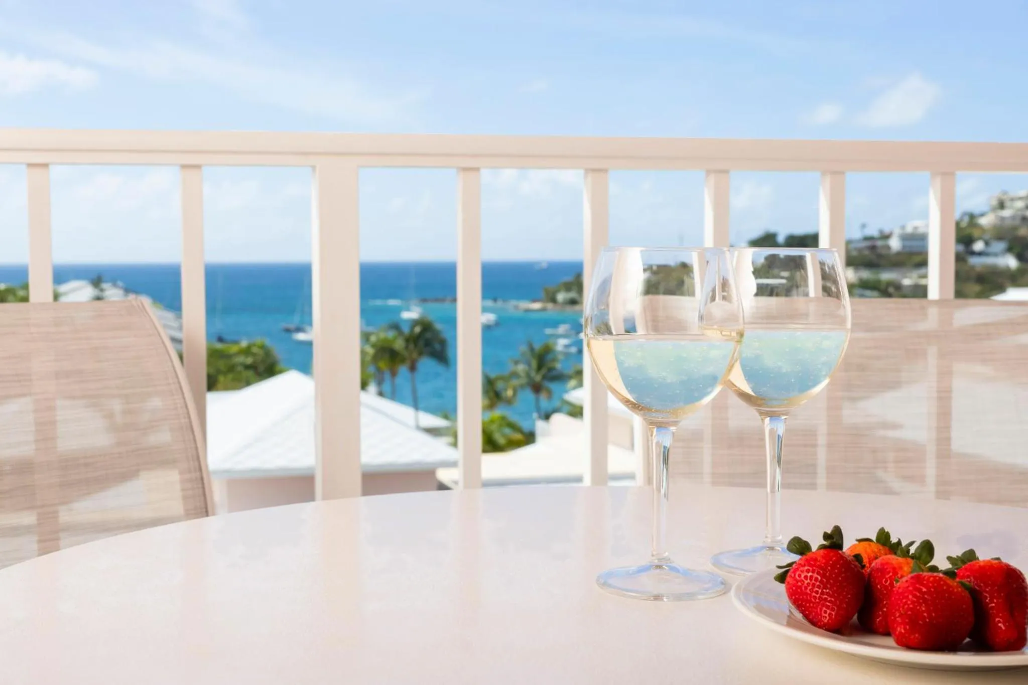 Deux verres de vin et des fraises sur une table en extérieur avec vue sur la mer.
