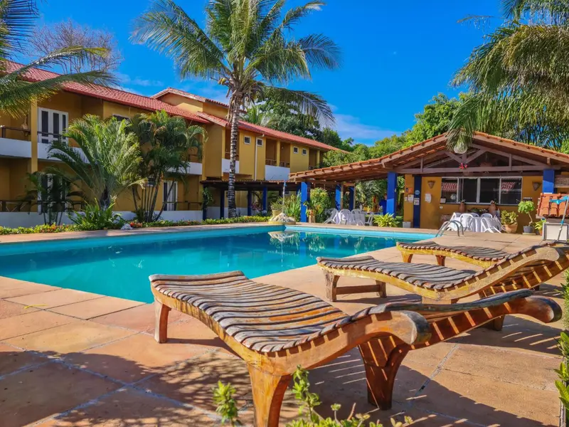 Transats en bois au bord d'une piscine turquoise dans un complexe hôtelier tropical.