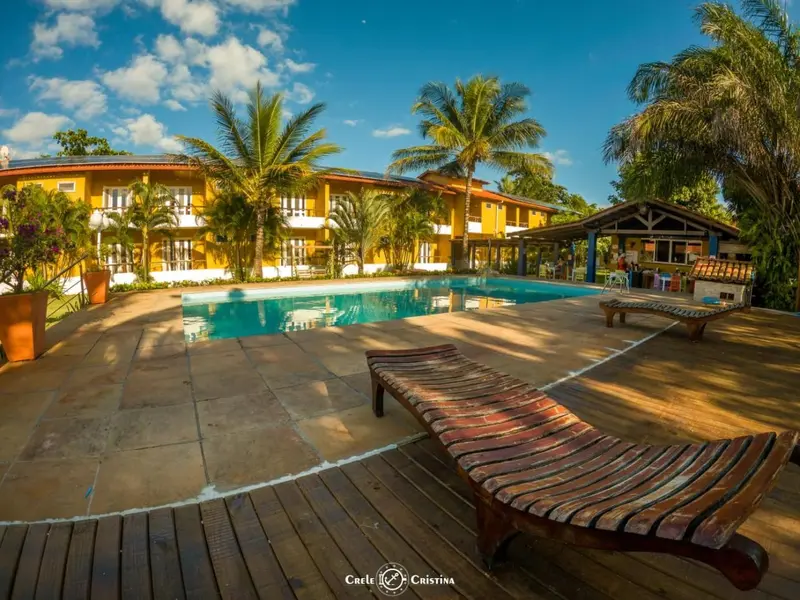 Bâtiment jaune bordant une piscine ensoleillée et une terrasse en bois.