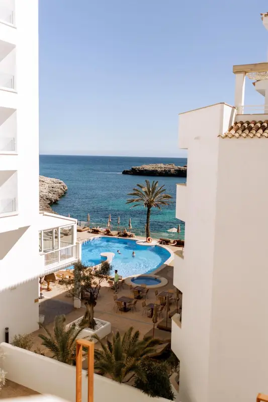 Vue aérienne sur une piscine d'hôtel bordée de palmiers et donnant sur la mer.