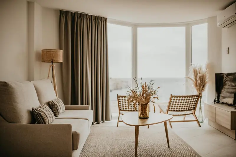 Un salon lumineux avec canapé et fauteuils face à une baie vitrée.