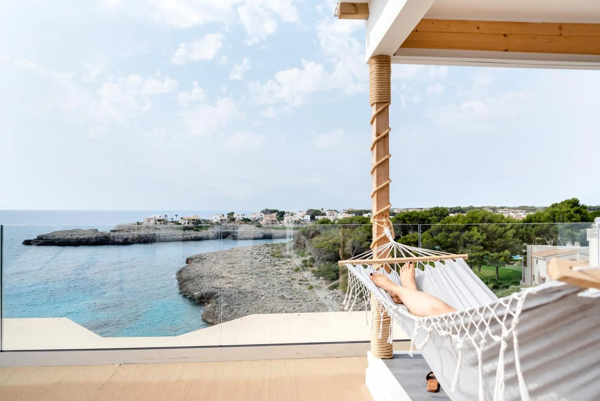 Une personne se détend dans un hamac sur une terrasse avec vue sur la mer.