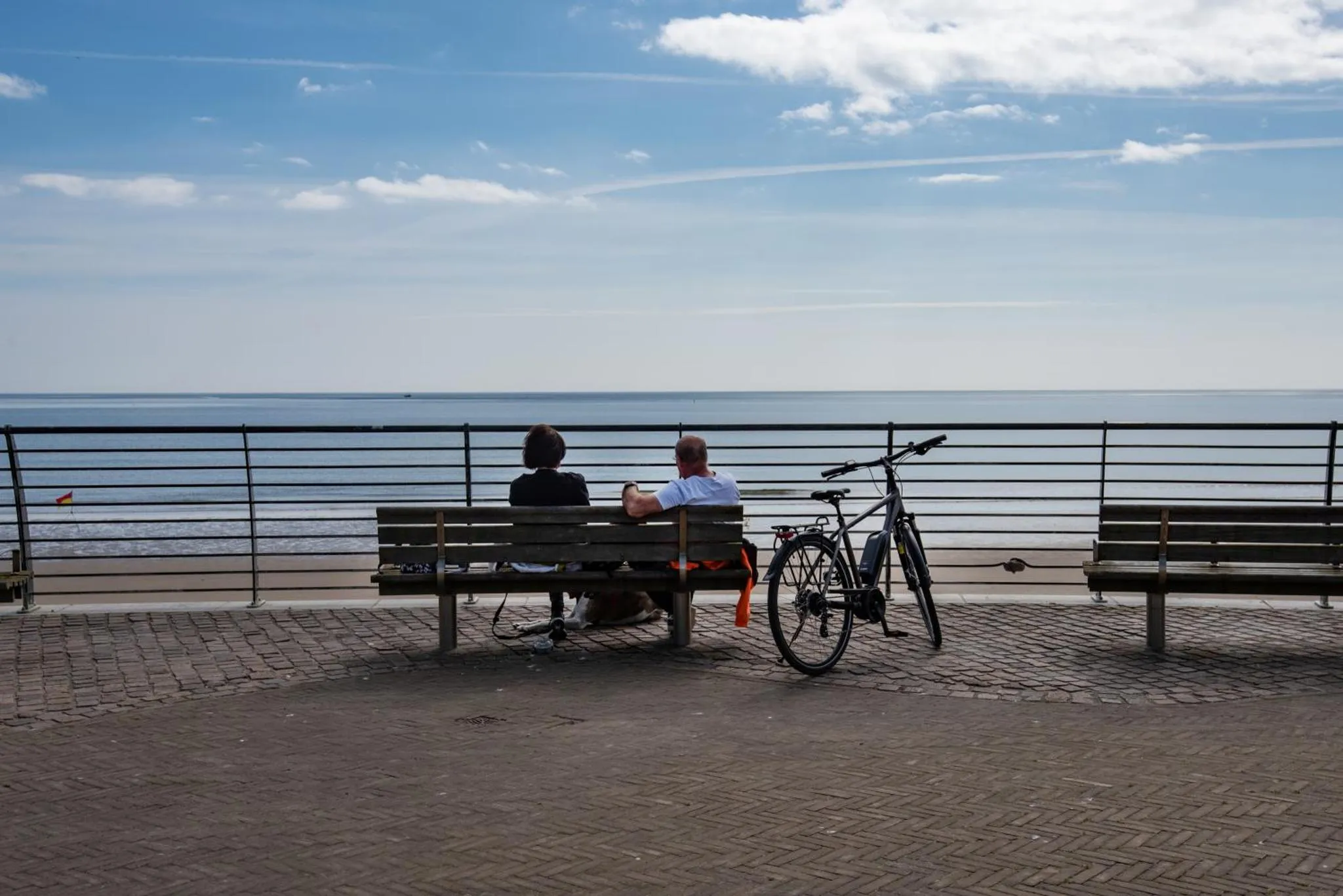 Deux personnes assises sur un banc face à la mer, avec un vélo à proximité.