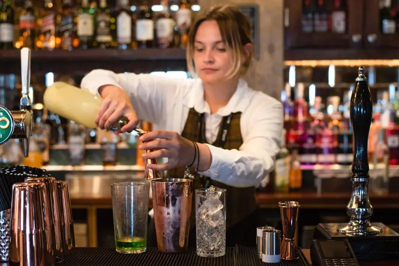 Une personne prépare une boisson derrière un comptoir de bar.