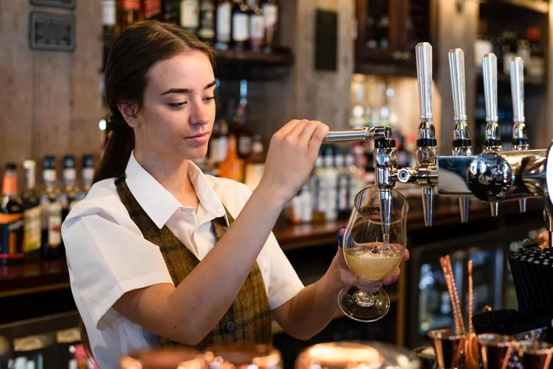 Une serveuse tire une bière à la pression derrière un comptoir de bar.