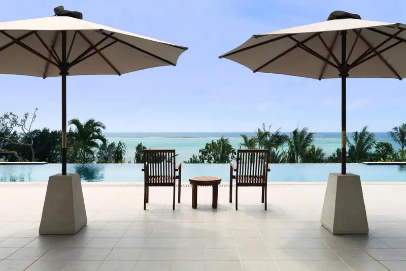 Deux fauteuils et une table basse se trouvent au bord d'une piscine à débordement avec vue sur la mer.