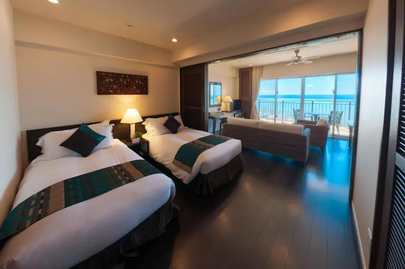 Chambre lumineuse avec deux lits et accès à une terrasse vue sur mer.