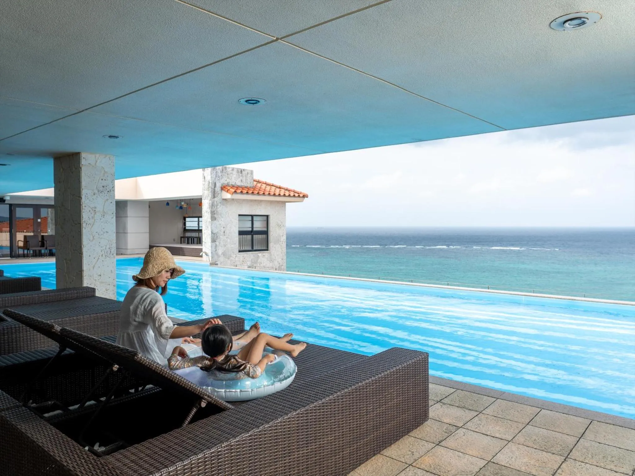 Une femme et un enfant se reposent au bord d'une piscine à débordement avec vue sur l'océan.