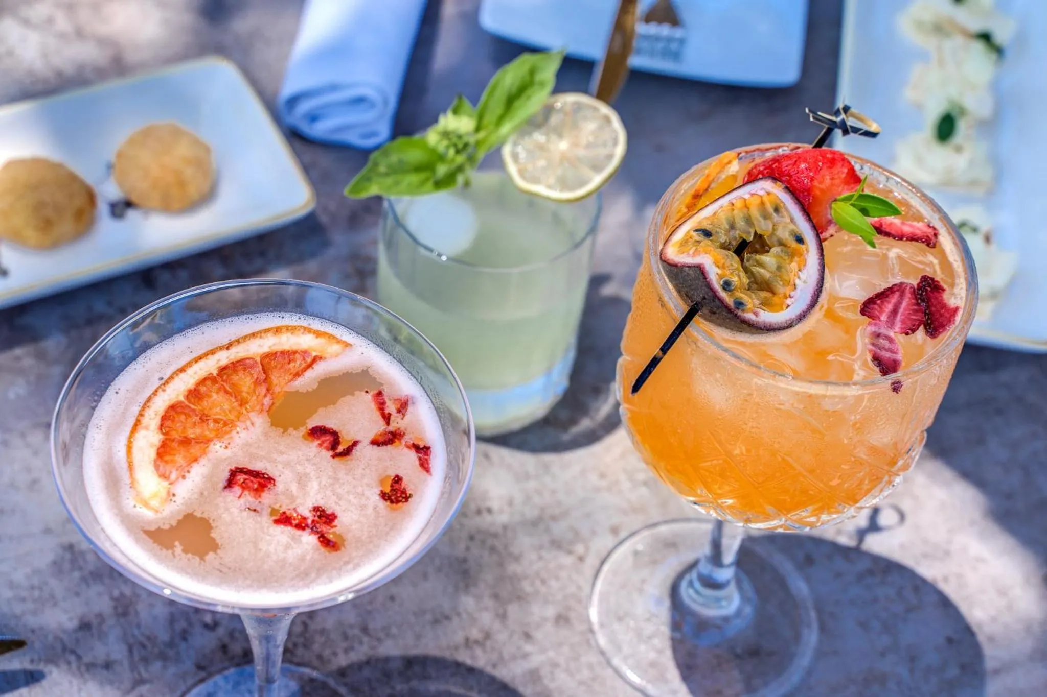 Trois cocktails colorés et des amuse-gueules sont présentés sur une table.
