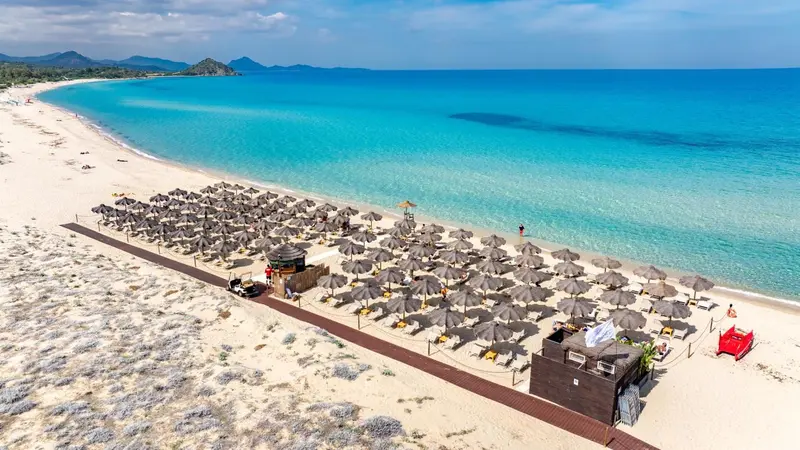 Vue aérienne d'une plage de sable fin bordée de parasols et de chaises longues.