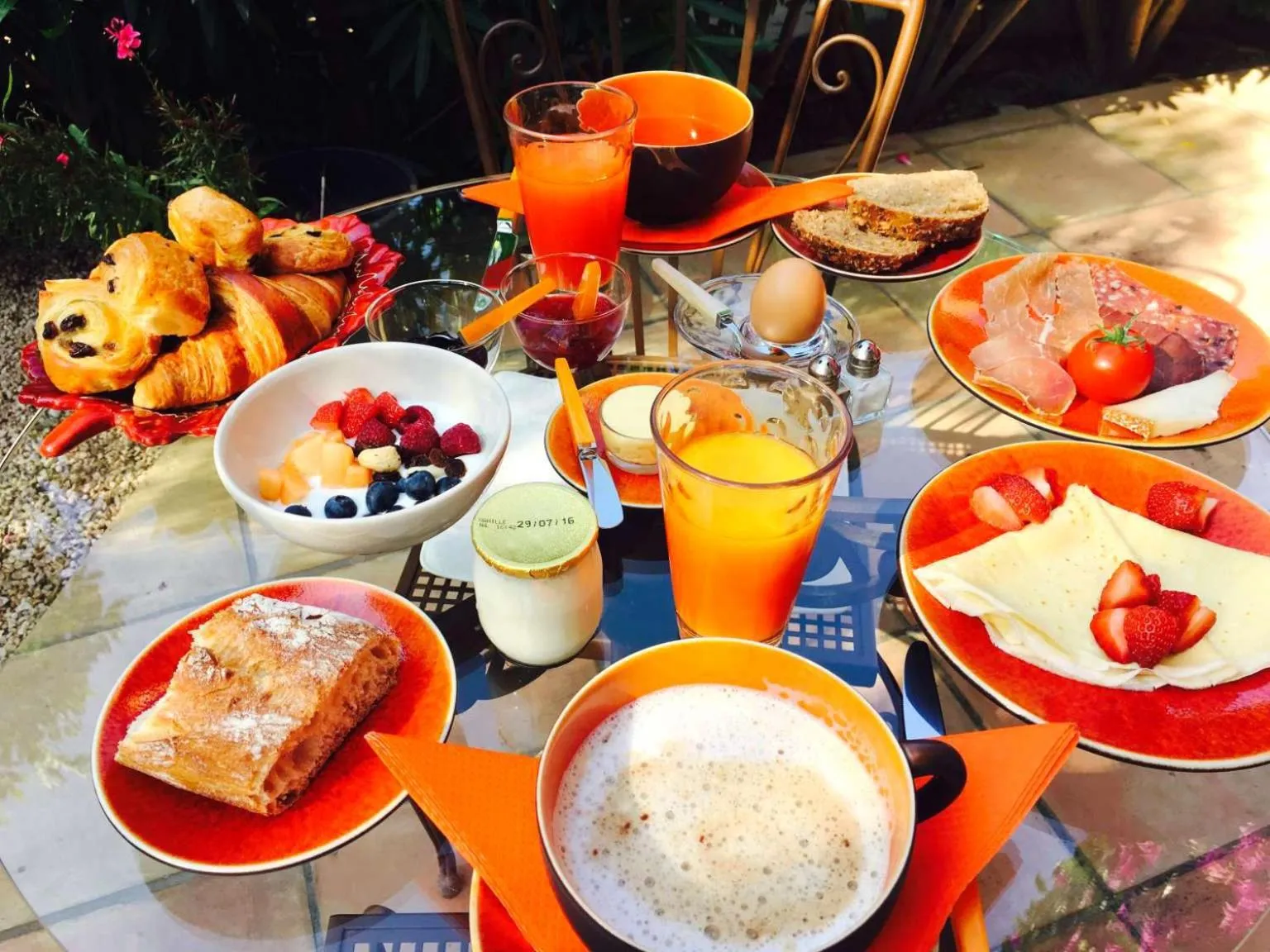 Une table est dressée pour un petit-déjeuner avec des viennoiseries, des fruits et des boissons.