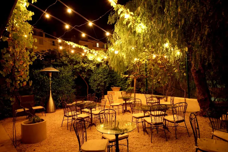 Terrasse illuminée avec tables et chaises sous des guirlandes lumineuses.
