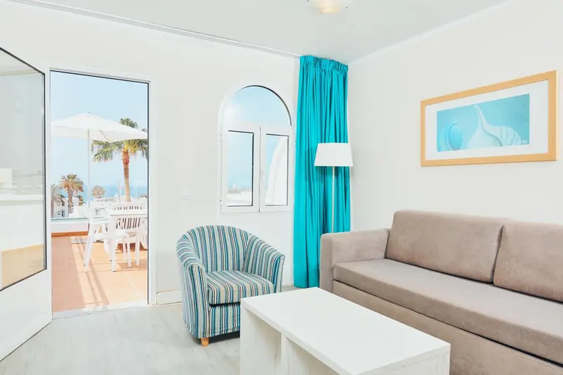 Espace de détente lumineux avec canapé et fauteuil face à une terrasse ensoleillée.