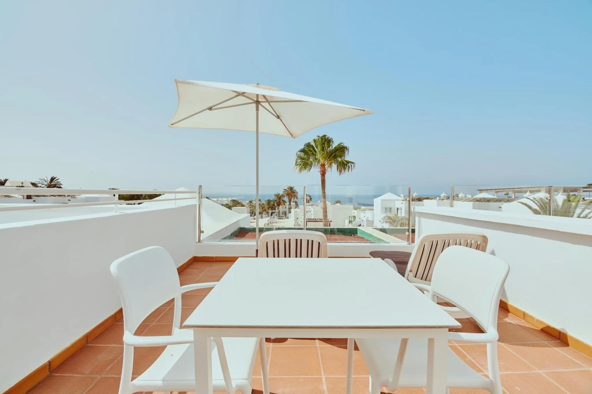 Terrasse aménagée avec table et chaises, vue sur la mer et la végétation.