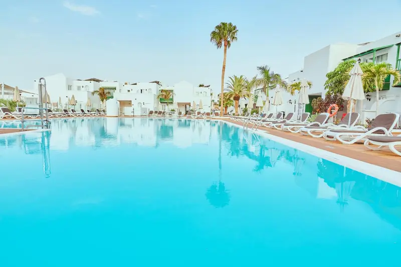 Une piscine turquoise reflète les palmiers et les bâtiments blancs environnants.