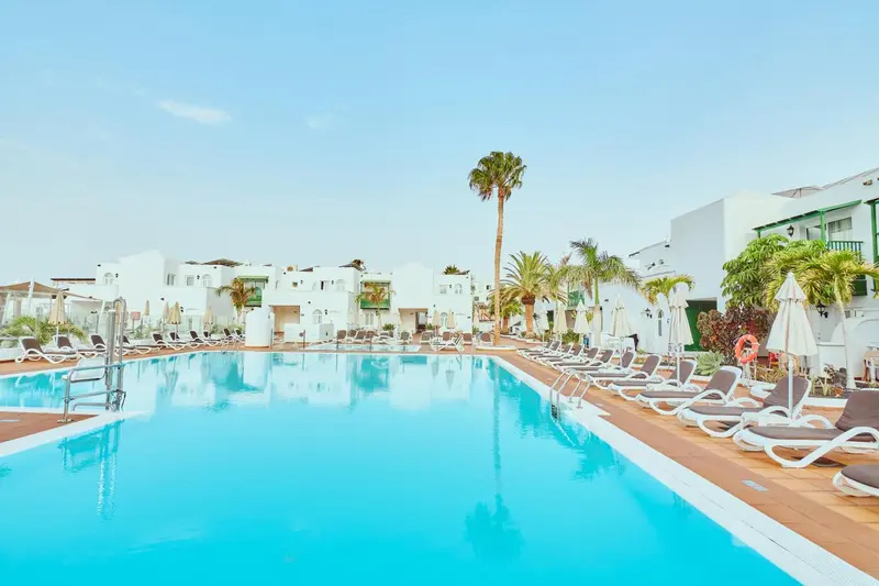 Une piscine rectangulaire bordée de transats blancs sous le soleil.