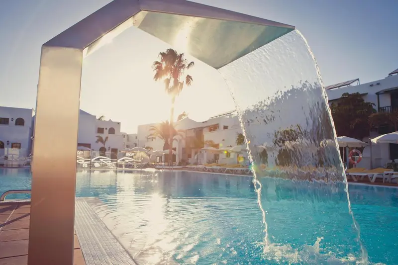 Une cascade d'eau se déverse dans une piscine turquoise au bord d'un complexe hôtelier.