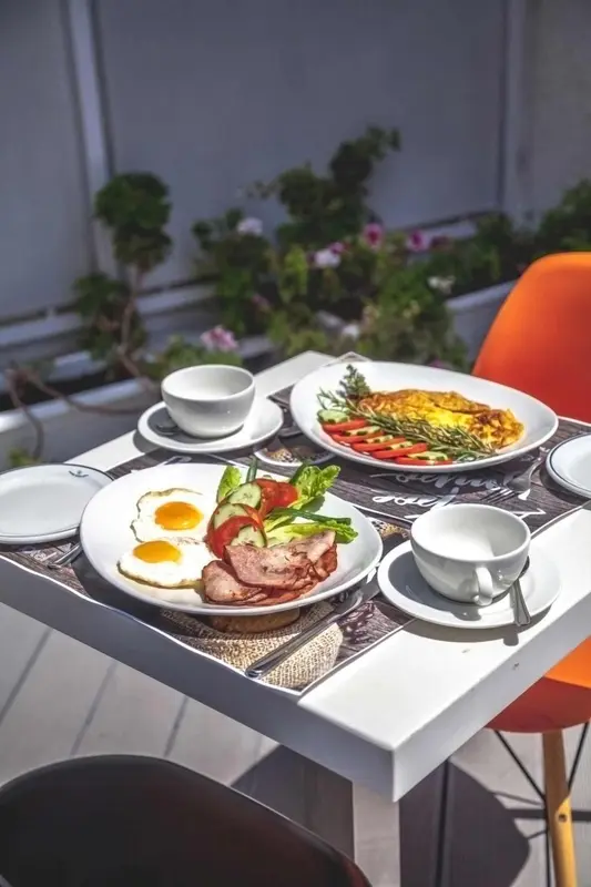 Une table blanche est dressée avec un petit-déjeuner copieux sur une terrasse ensoleillée.
