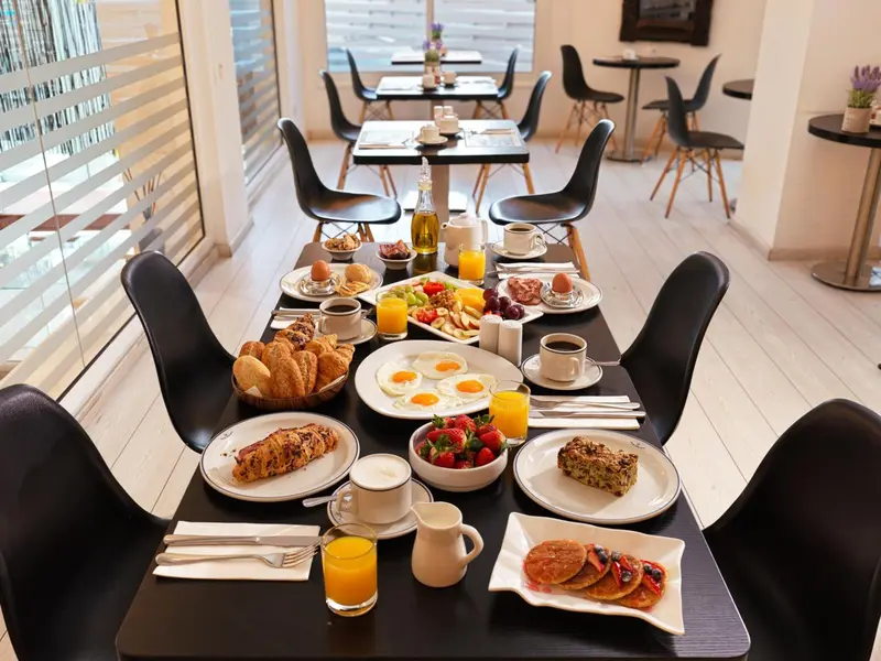 Une table est dressée pour un copieux petit-déjeuner avec des viennoiseries, des fruits et des boissons.