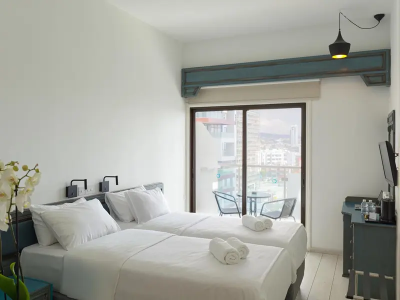 Une chambre lumineuse avec un grand lit et un balcon donnant sur la ville.
