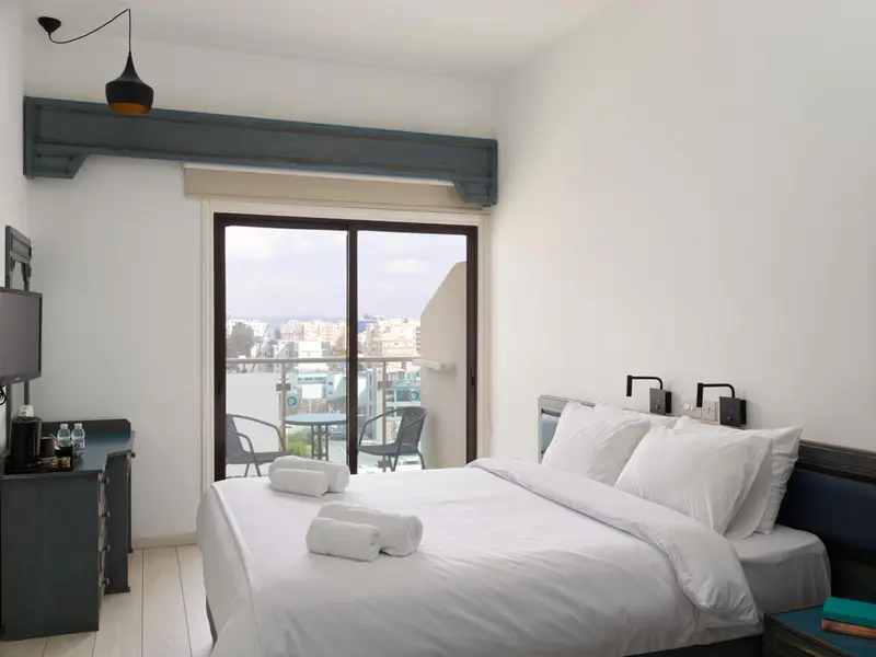 Une chambre lumineuse avec un grand lit et un accès à un balcon.