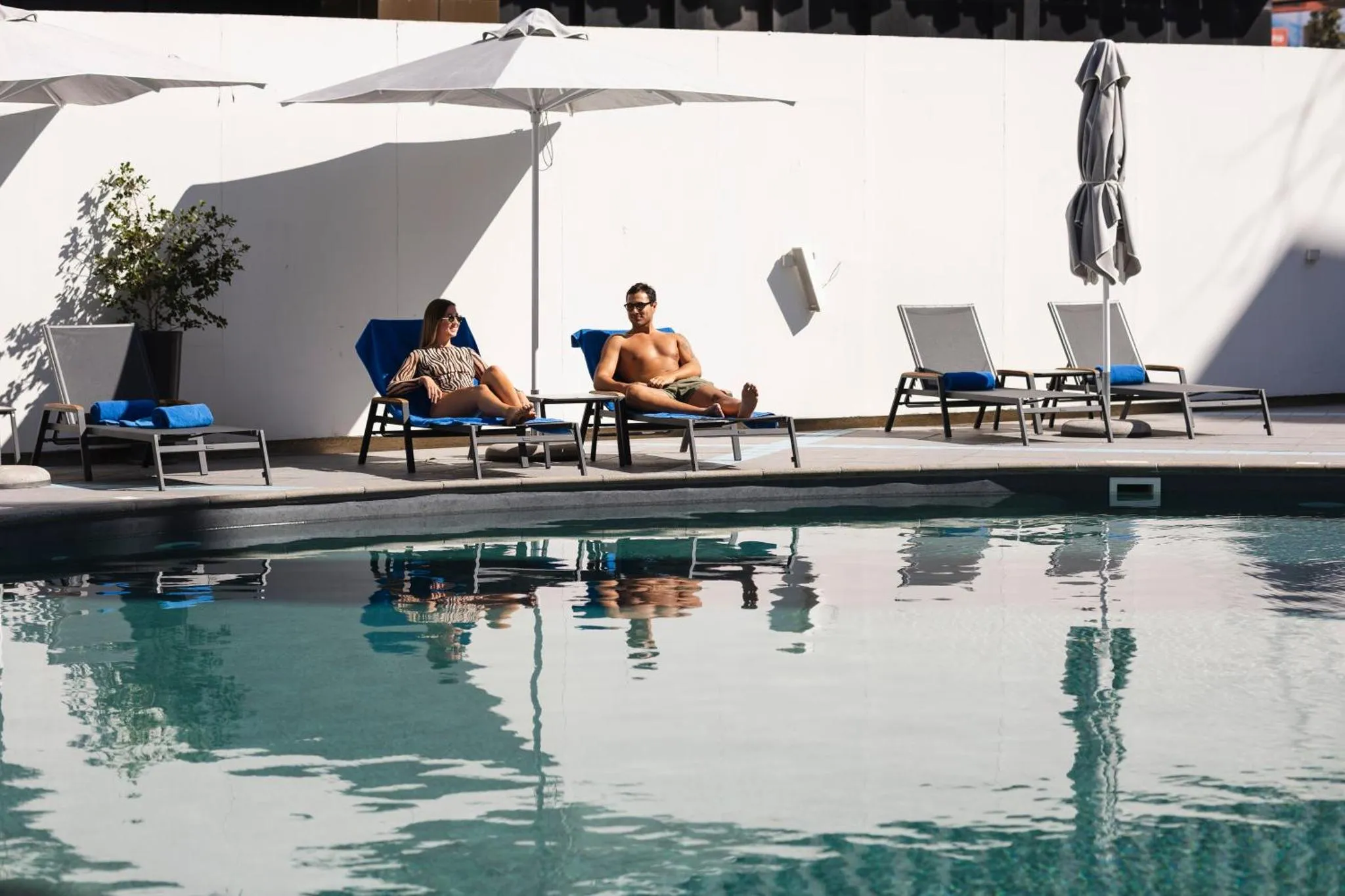 Deux personnes se relaxent sur des transats au bord d'une piscine ensoleillée.