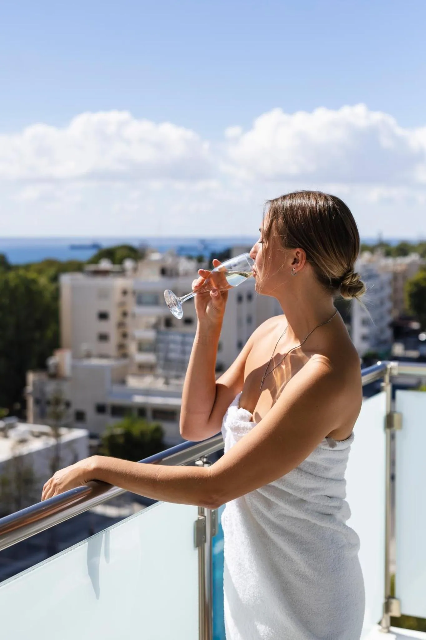 Une femme boit une boisson sur une terrasse avec vue sur la ville et la mer.