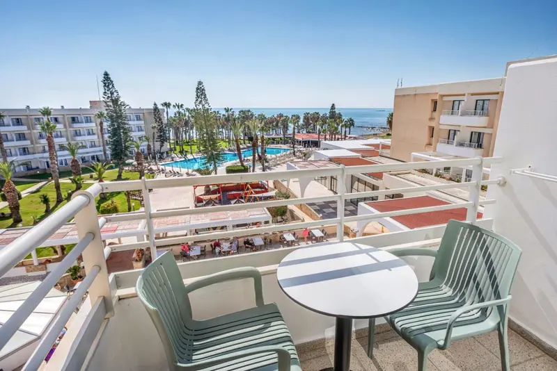 Vue d'un balcon avec mobilier vert donnant sur une piscine et la mer.