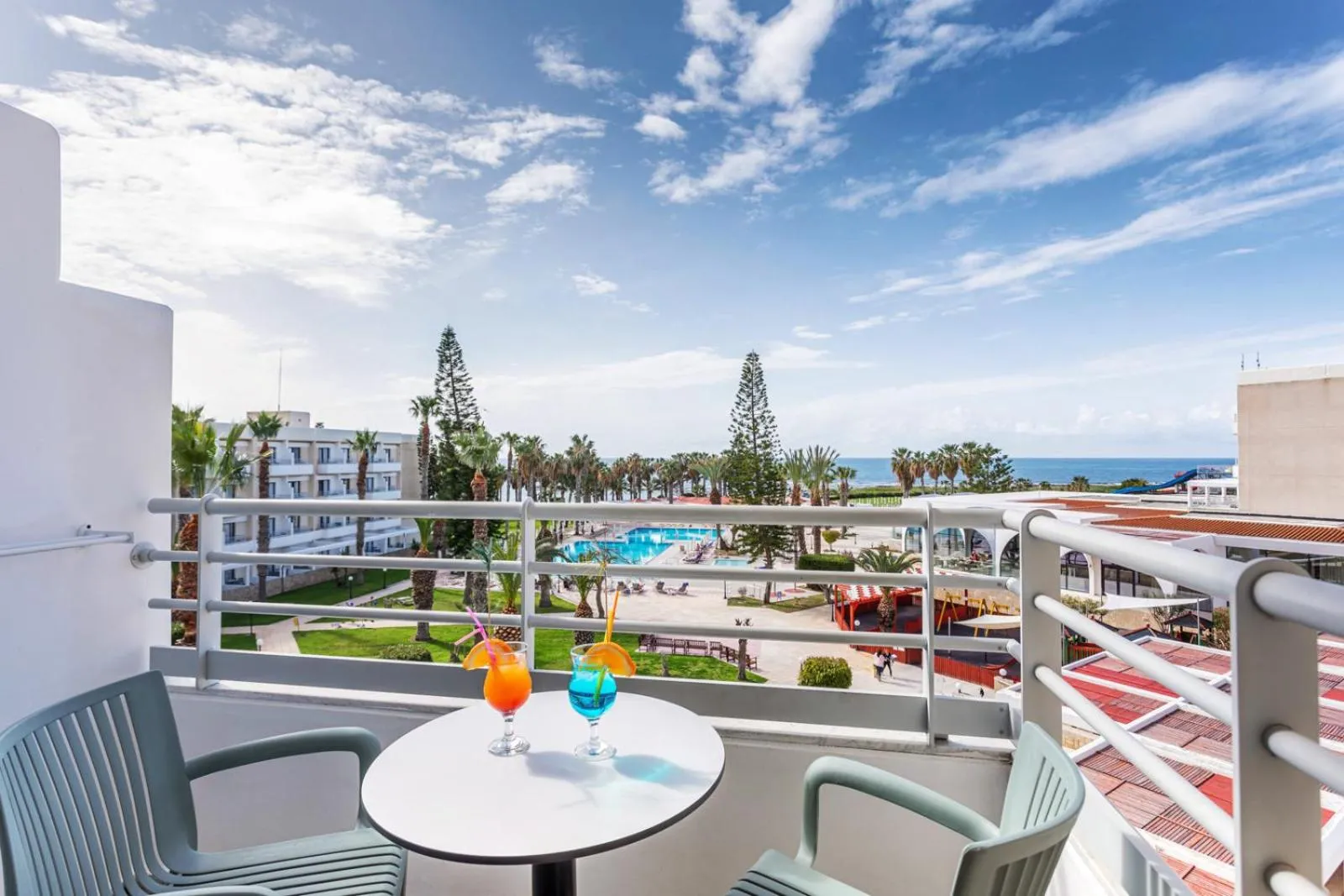Terrasse avec table basse et boissons, vue sur une piscine et la mer.