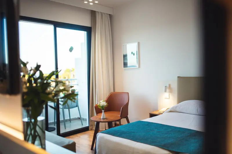 Une chambre lumineuse avec un lit et un fauteuil près d'une baie vitrée.
