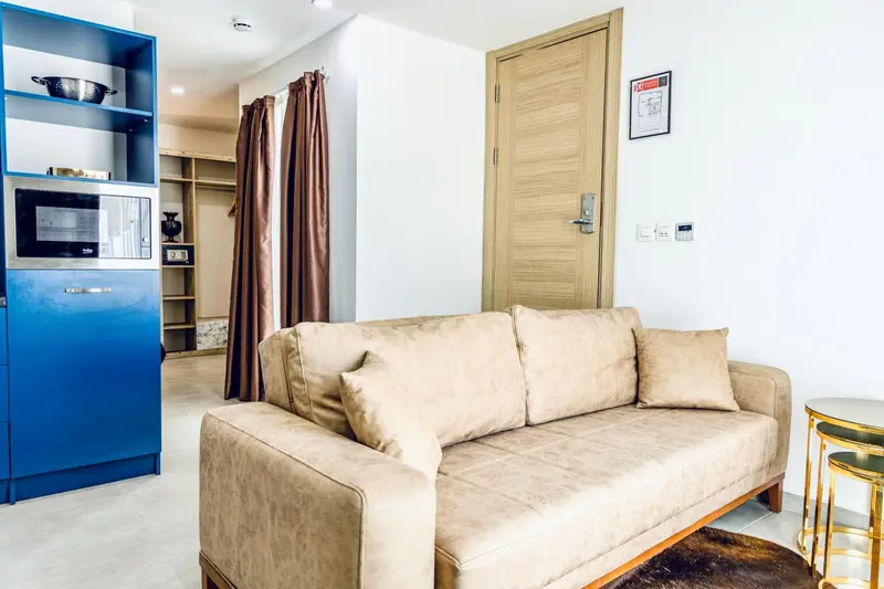 Un canapé beige dans un espace de vie lumineux avec une kitchenette bleue.