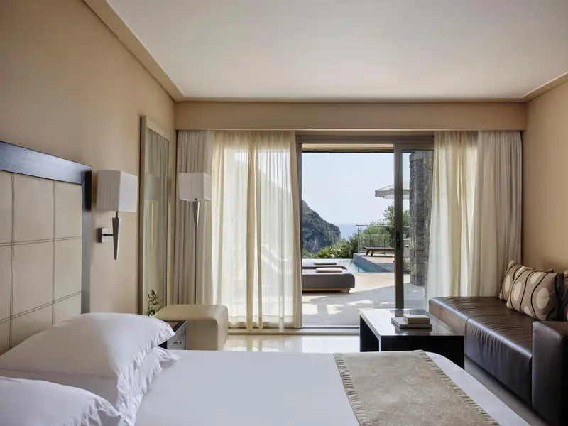 Chambre lumineuse avec un canapé et une vue sur une piscine et la mer.