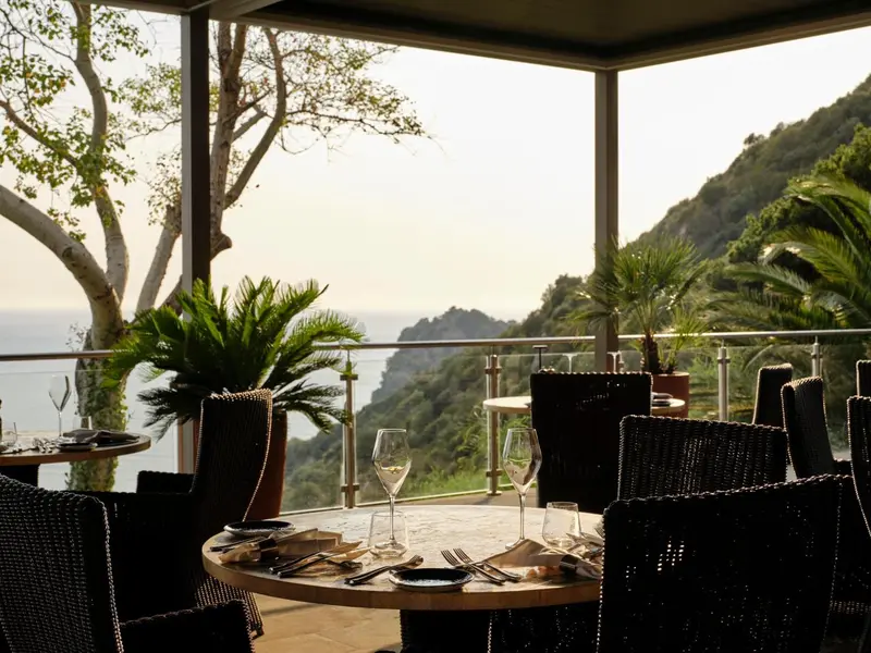 Une table est dressée sur une terrasse avec vue sur la mer et les collines.