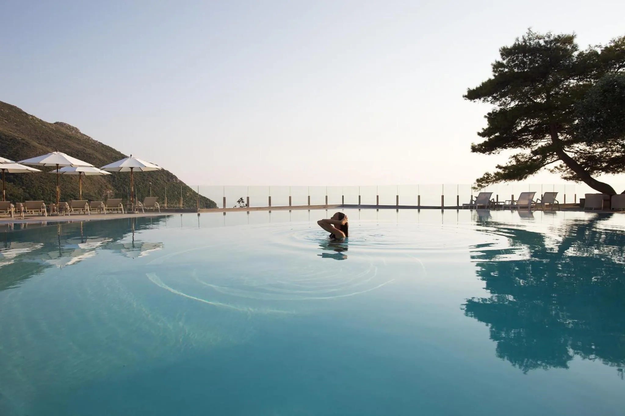 Une personne nage dans une piscine à débordement avec vue sur la mer.