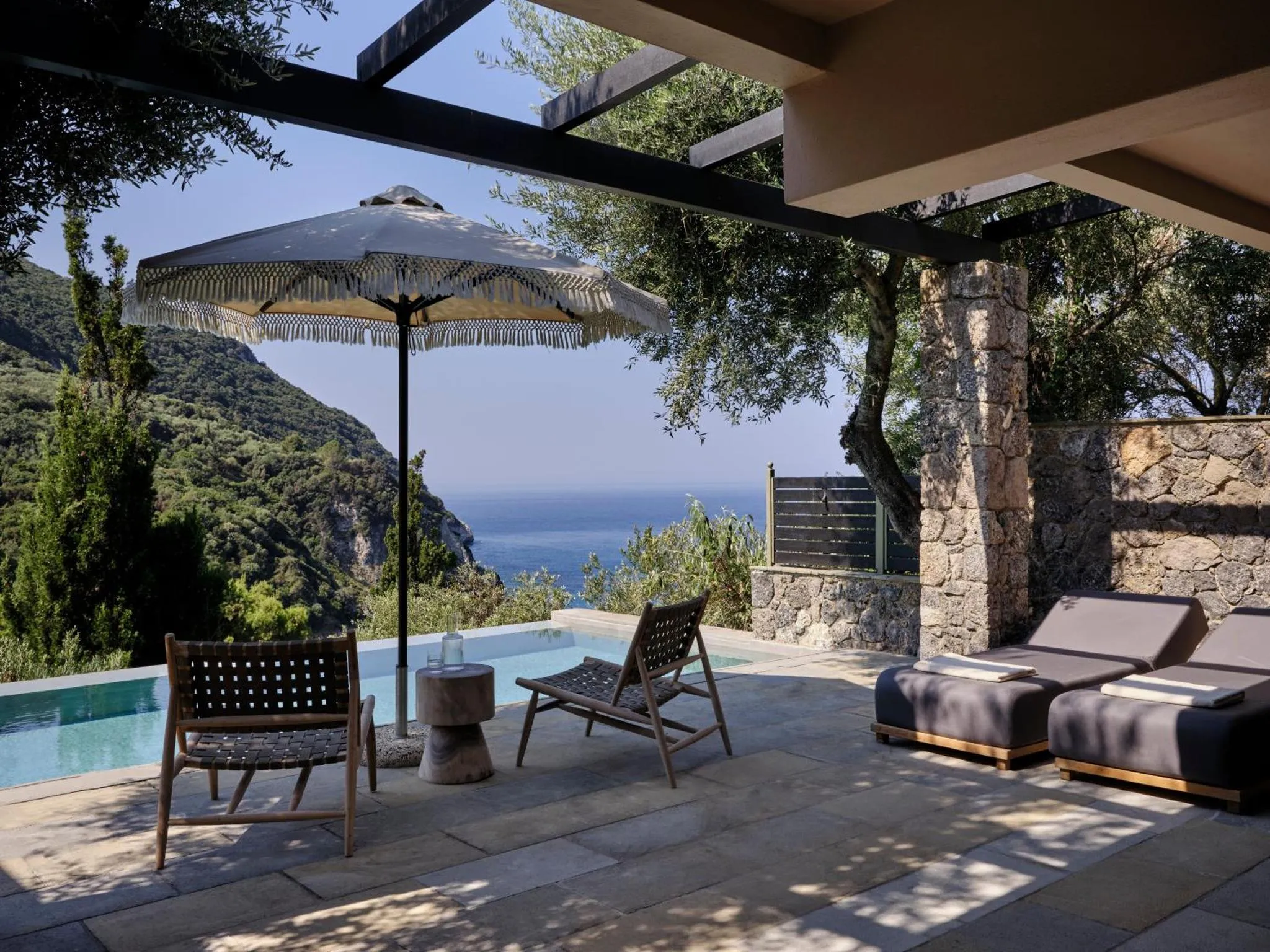 Deux fauteuils et des chaises longues invitent à la détente sur une terrasse avec piscine et vue sur la mer.