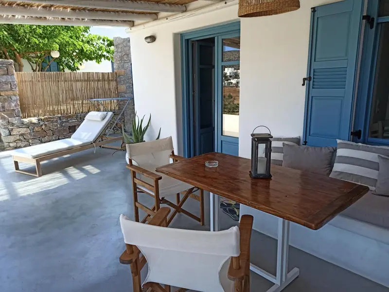 Espace extérieur aménagé avec table, chaises et transats devant une ouverture bleue.