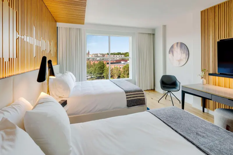 Une chambre lumineuse avec deux lits simples et une vue sur la ville.