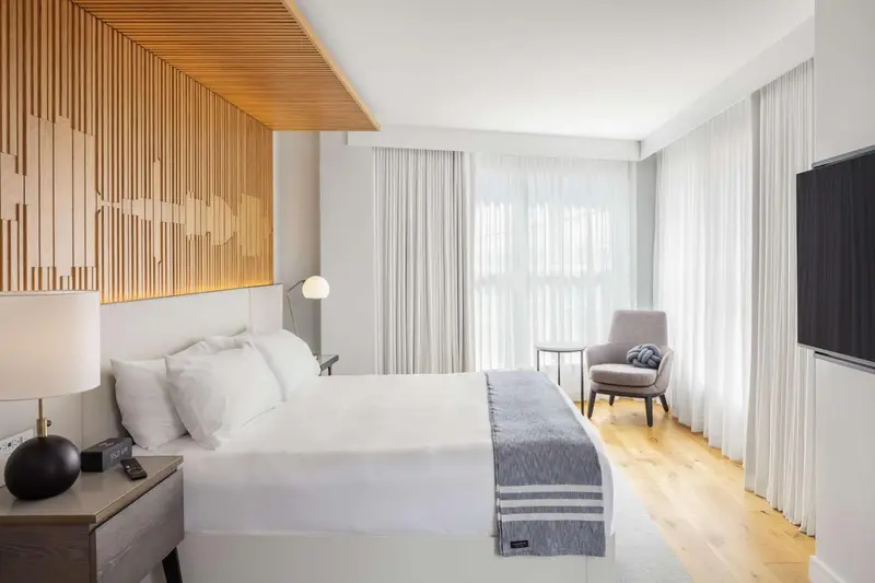 Chambre lumineuse avec un grand lit et un fauteuil près d'une fenêtre.