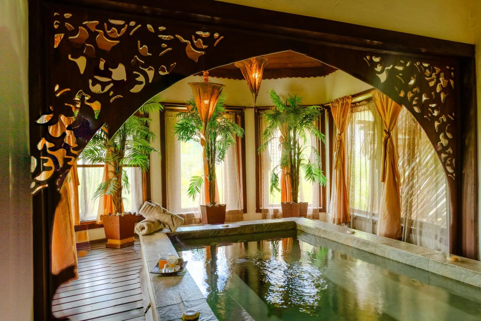 Espace de détente intérieur avec piscine et végétation tropicale.