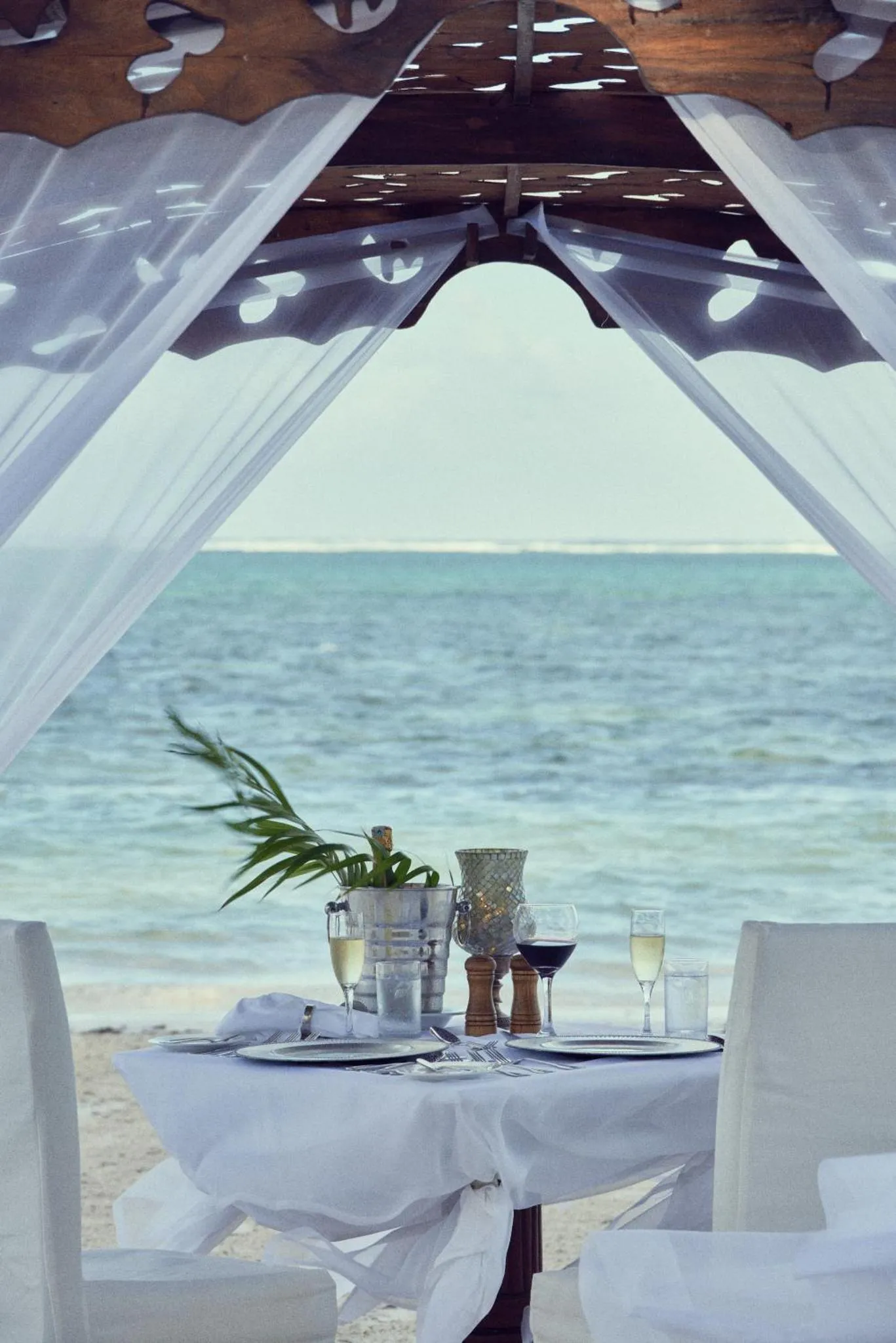 Une table dressée sur une plage de sable blanc offre une vue sur la mer turquoise.