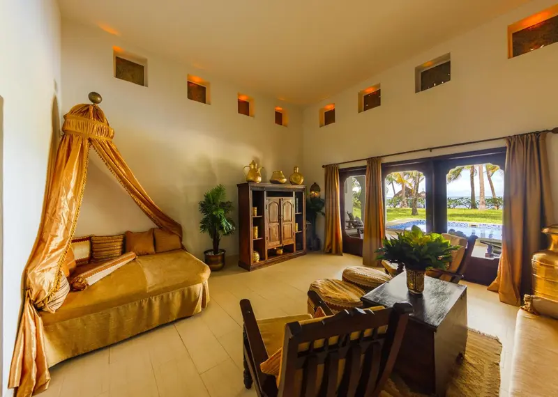 Espace de détente intérieur avec un lit à baldaquin et vue sur une piscine et la mer.