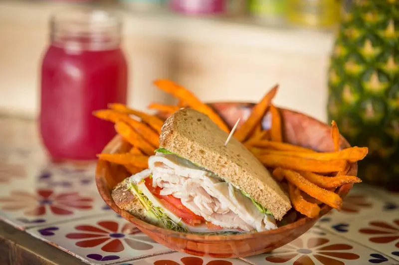 Un sandwich et des frites de patates douces sont servis dans un bol en bois sur une table colorée.