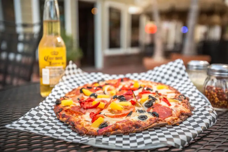 Une pizza colorée est présentée sur une table en extérieur avec une bière.
