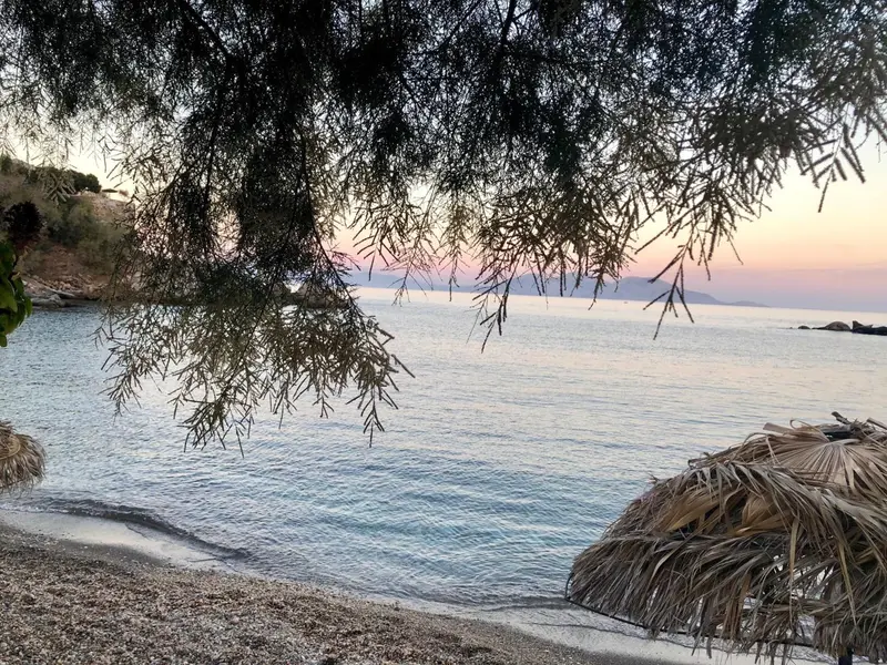 Une plage de galets bordée d'une mer calme au coucher du soleil.