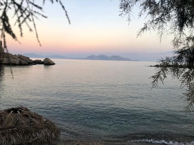Ciel pastel au coucher du soleil sur une mer calme et une côte rocheuse.