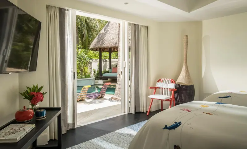 Une chambre lumineuse s'ouvre sur une piscine et un jardin tropical.