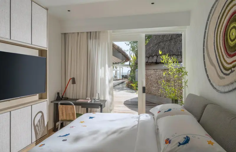 Une chambre lumineuse s'ouvre sur une terrasse avec vue sur la végétation.