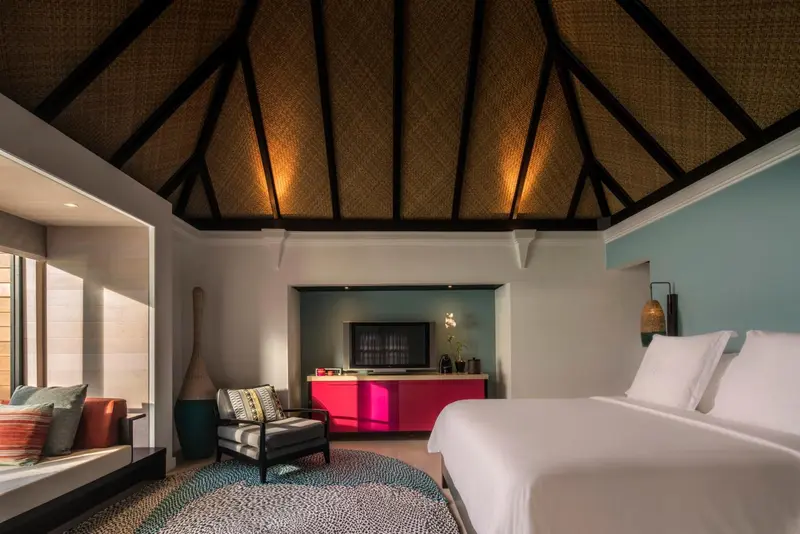 Intérieur d'une chambre avec un lit blanc et un coin salon coloré.